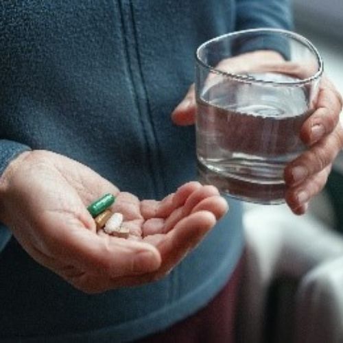 A person holding a glass of water in one hand and a couple of tablets in the other