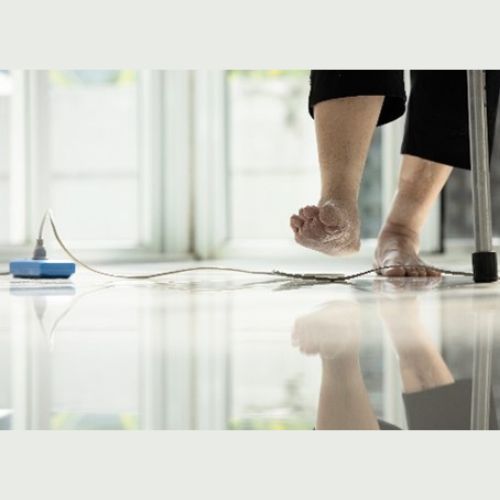 An elderly person using a walking aid steps near a cord lying on a shiny floor, highlighting a potential tripping hazard in a home environment