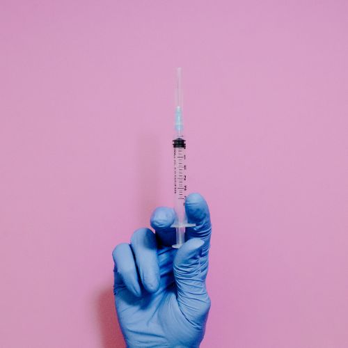 hand holding a single syringe on a pnk background