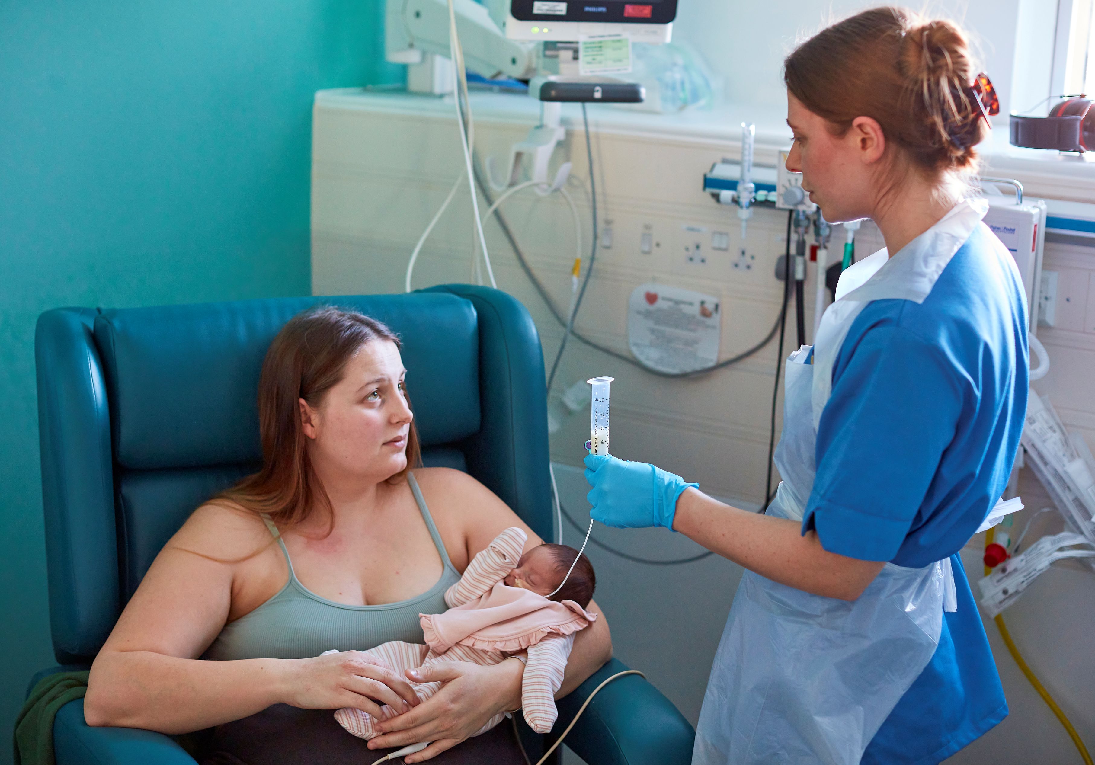 female patient sat on chair, holding her newborn baby and listening carefully to a nurse