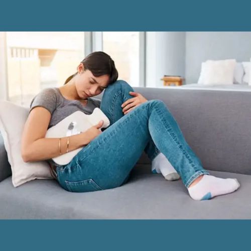 Woman sitting on a couch holding a heating pad against her stomach for menstrual pain relief.