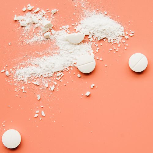 Crushed white tablets on a pastel orange background